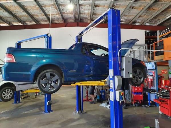 Blue utility vehicle lifted on a hydraulic hoist inside a mechanical workshop.