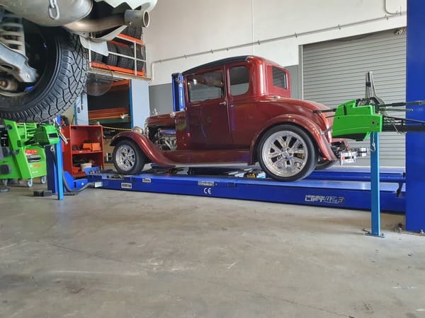 Classic red car on a wheel alignment machine inside an auto workshop.