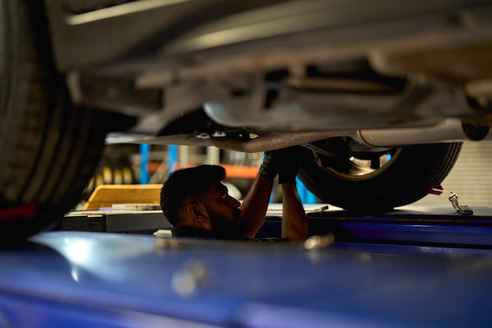 Technician under a raised vehicle, loosening a bolt.