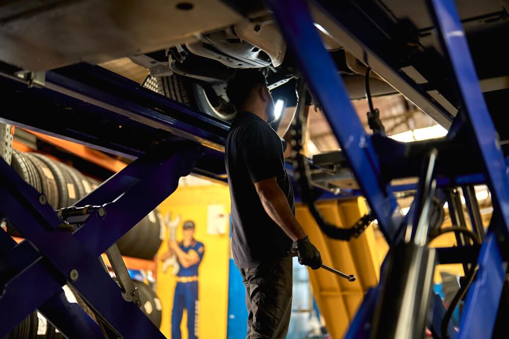 Service technician inspecting underside of a raised vehicle.
