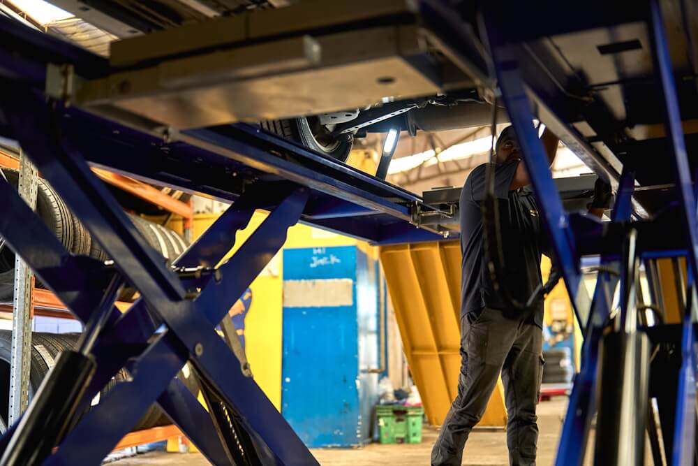 Service technician inspecting underside of a raised vehicle.