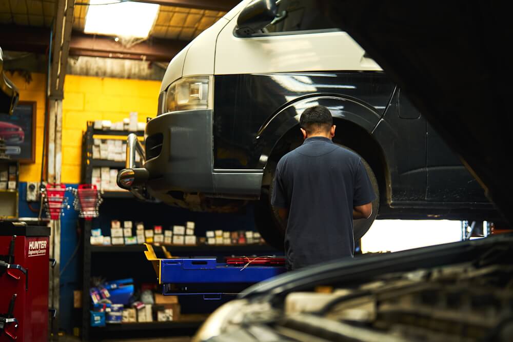 Service technician inspecting tyre on the side of a raised white van.