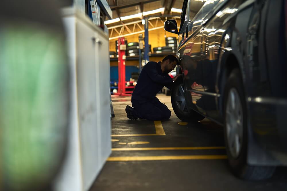 Service technician inspecting underside of a raised vehicle.
